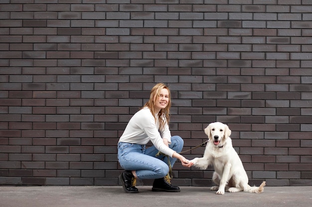 Jeune belle fille avec un chien dans une rue contre un mur un chiot retriever donne une patte à une femme