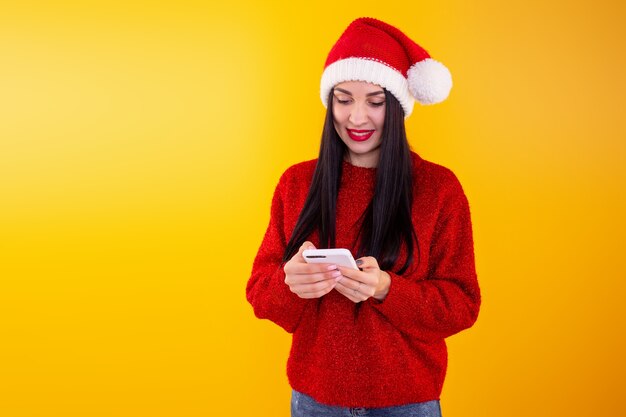 Jeune belle fille dans un bonnet de Noel rouge tient un téléphone dans ses mains contenu de réduction de Noël