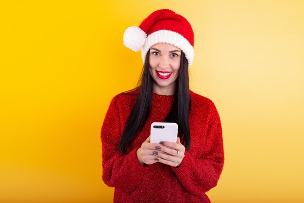 Jeune belle fille dans un bonnet de Noel rouge tient un téléphone dans ses mains