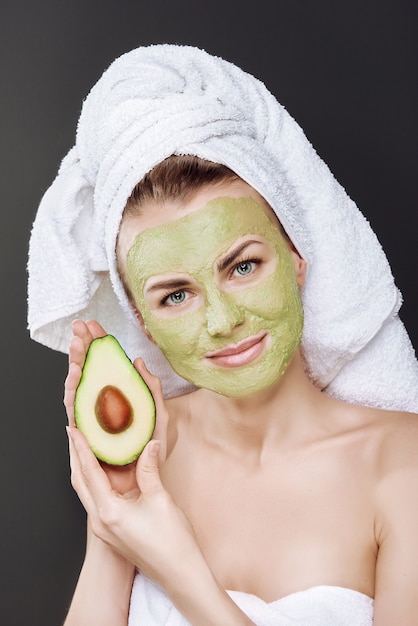 Jeune belle fille dans une serviette blanche sur la tête avec un masque cosmétique d'avocat sur son visage.