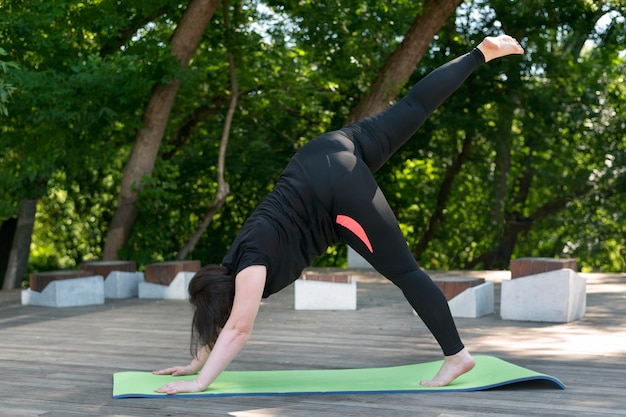 Jeune belle fille effectue une pose de yoga modifiée museau de chien vers le bas. Activités extérieures. La fille potelée mène un mode de vie sain