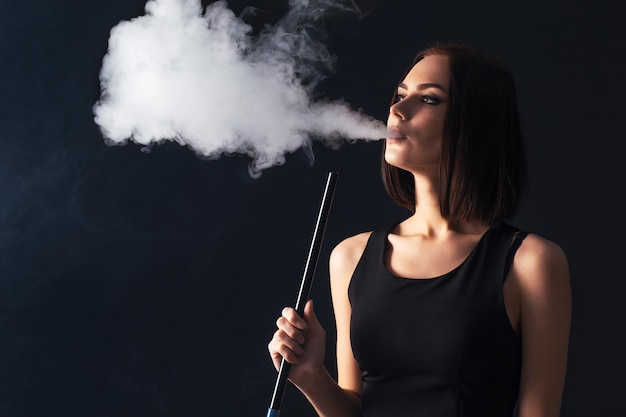 Jeune et belle fille fume un narguilé. Il produit de la fumée par sa bouche.