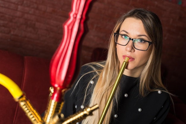 La jeune belle fille fume un narguilé