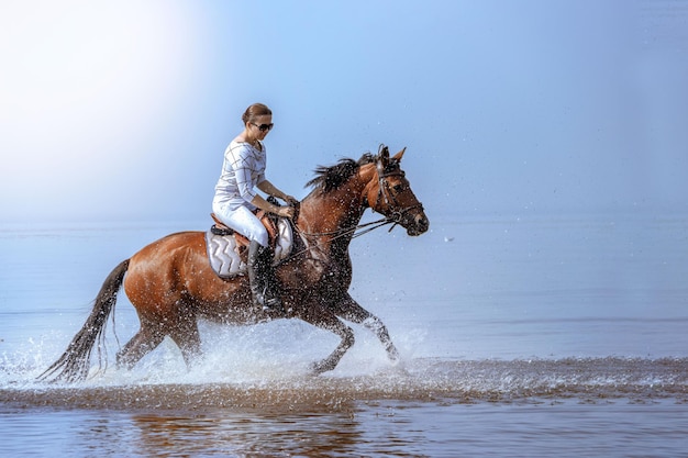 La jeune belle fille galope très vite sur l'eau un jour ensoleillé chaud