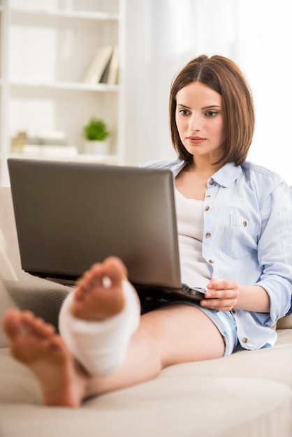 Jeune belle fille avec des gyps sur la jambe, assis sur le canapé.