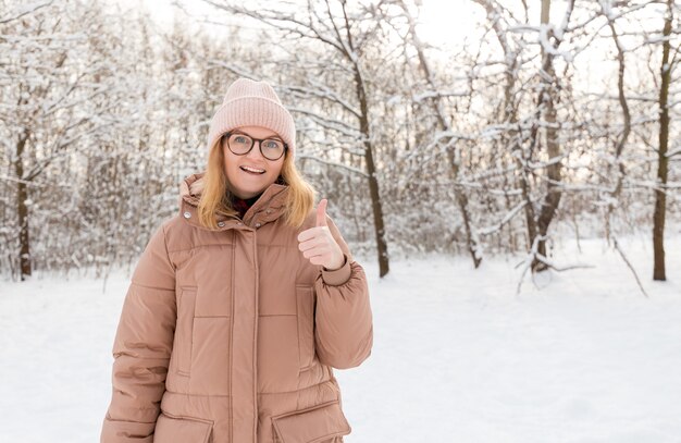 Jeune belle fille heureuse en bonnet d'hiver posant dans la forêt d'hiver. Fond de neige