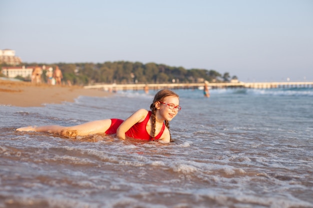 Jeune belle fille à lunettes et un maillot de bain rouge se trouve sur la plage et joue dans les vagues