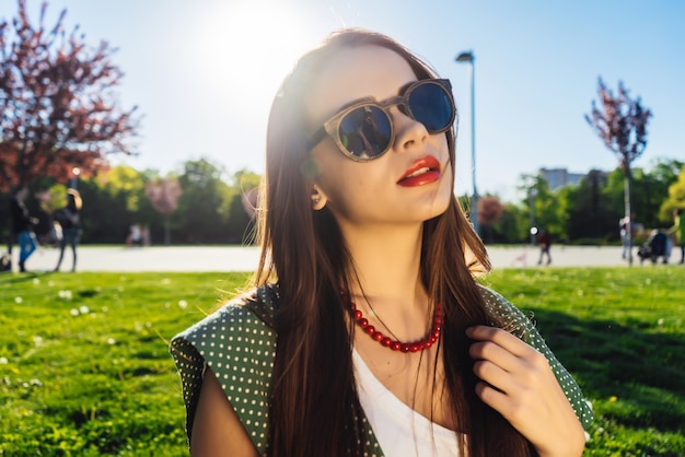 Jeune belle fille à lunettes de soleil marchant dans le parc par une journée ensoleillée, profitant de la nature