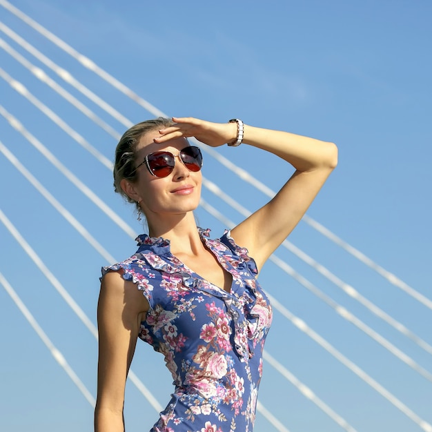 Jeune belle fille à lunettes de soleil en regardant le soleil sur le fond de ciel bleu