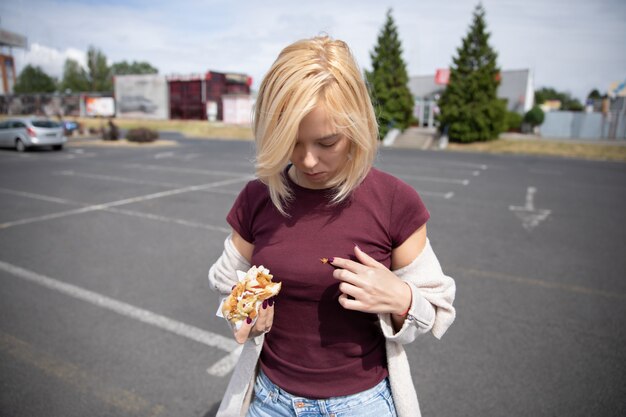 Jeune belle fille, manger des hot-dogs sur le parking. Vêtements souillés à cause de l'inexactitude.