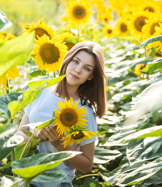 Jeune belle fille marche en été dans un champ avec des tournesols en fleurs