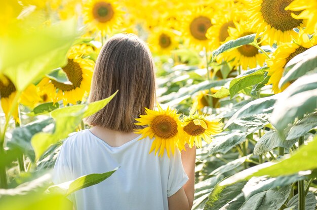 Jeune belle fille marche en été dans un champ avec des tournesols en fleurs