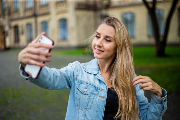 Jeune belle fille à la mode moderne dans une veste en jean fait un selfie au téléphone