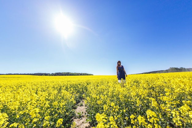 Jeune belle fille modèle de grande taille heureuse en robe bleue sur un champ de colza en fleurs en été Suivez-moi concept