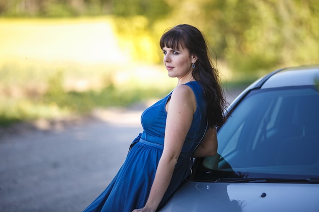 Jeune belle fille modèle grande taille heureuse en robe bleue près de sa voiture