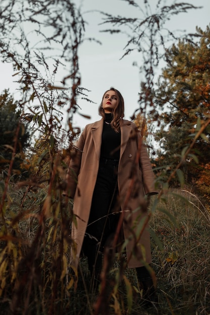 Jeune belle fille modèle à la mode dans un manteau beige élégant d'automne et un pull noir se promène dans la nature