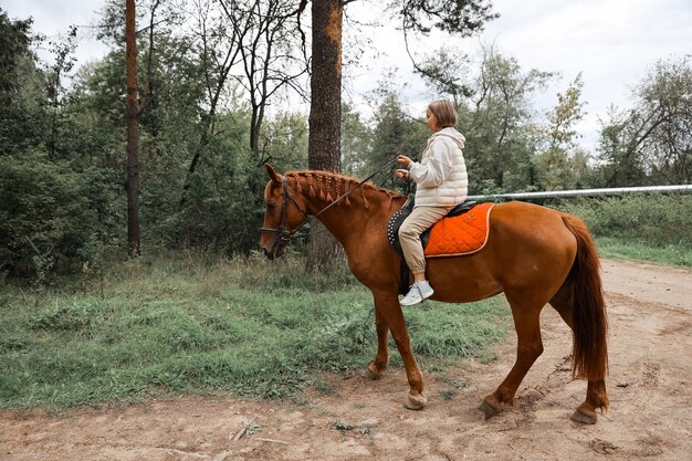 La jeune belle fille monte son cheval aux routes de campagne en automne