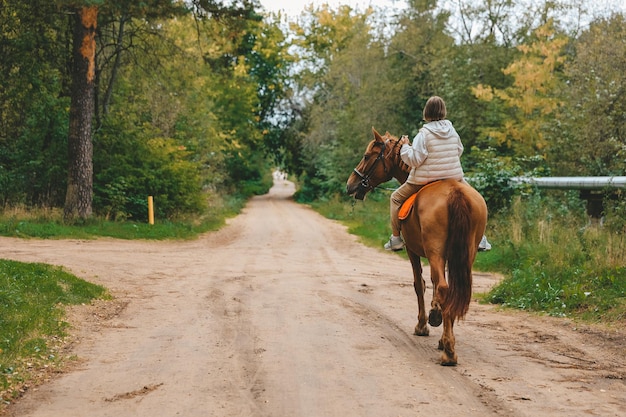 La jeune belle fille monte son cheval aux routes de campagne en automne