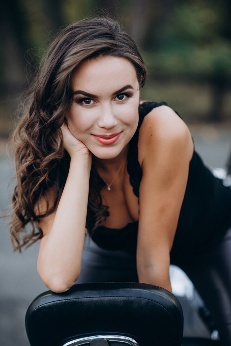 Photo jeune belle fille de motard dans un débardeur noir et un pantalon en cuir est assis sur une moto par derrière. le concept de vitesse et de liberté