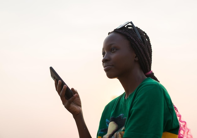 Jeune belle fille noire utilisant un téléphone intelligent sur la plage de la mer au coucher du soleil