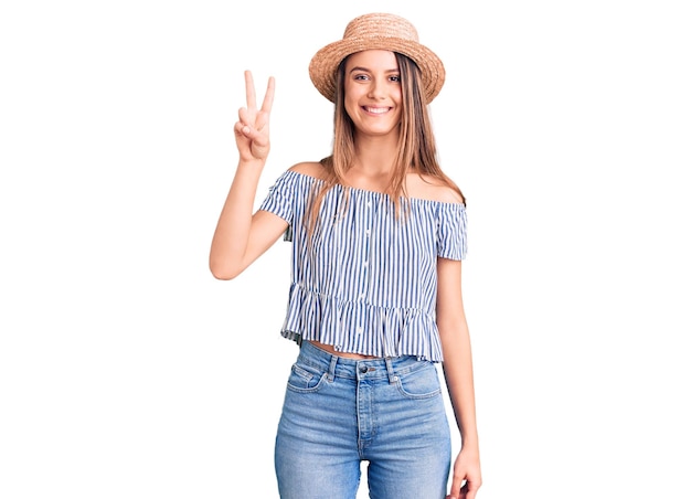 Jeune belle fille portant un chapeau et un t-shirt montrant et pointant vers le haut avec les doigts numéro deux tout en souriant confiant et heureux