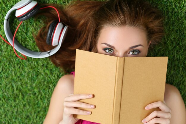 Jeune belle fille portant sur l'herbe dans le parc tenant un livre. Concept d'été, de loisirs et d'éducation. Vue de dessus