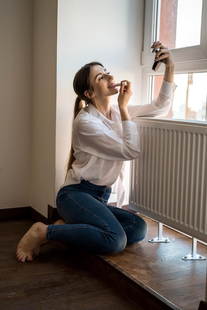 Jeune belle fille qui se maquille par la fenêtre le matin. concept de beauté