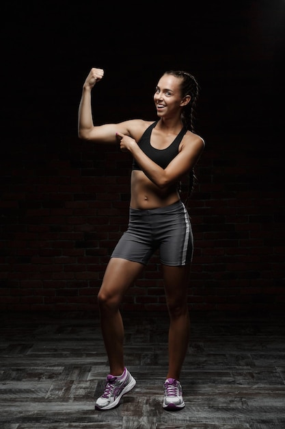 Jeune belle fille sportive souriante s'entraînant sur fond sombre