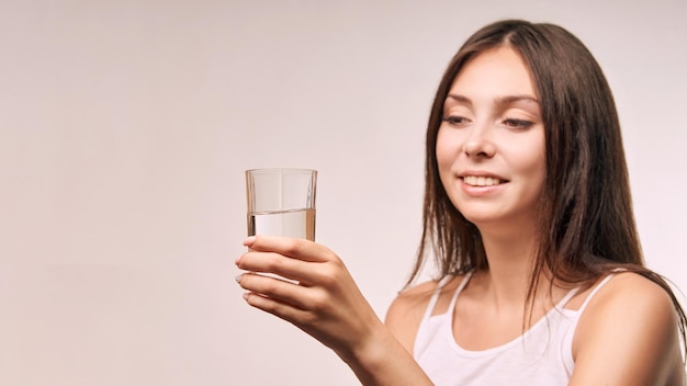 Jeune belle fille tenir un verre d'eau hydrater le visage féminin femmes heureuses à l'intérieur