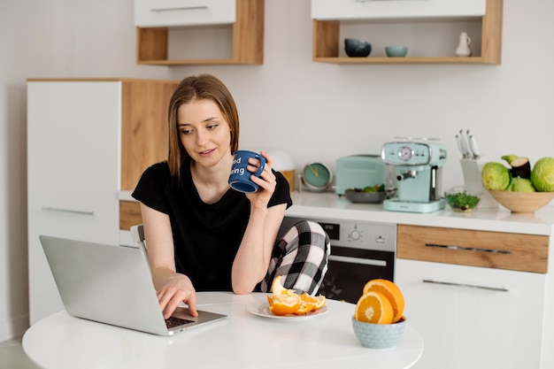 Jeune belle fille végétarienne habillée en pyjama mangeant des fruits et légumes pour le petit déjeuner à la maison dans la cuisine