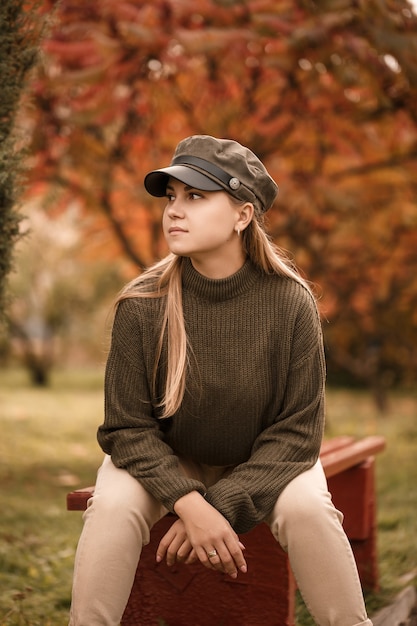 Jeune belle fille vêtue de vêtements élégants, pull vert et pantalon beige, dans un parc d'automne avec de beaux arbres