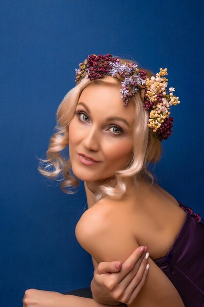 Jeune belle en fleurs dans une couronne de lilas aux lèvres délicates ravies sur fond bleu