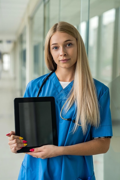 Une jeune belle infirmière se tient dans le couloir de l'hôpital et tient une tablette numérique. Notion de médecine