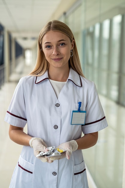 Jeune belle infirmière se tient dans le couloir avec un stéthoscope et des pilules dans ses mains Concept de médecine