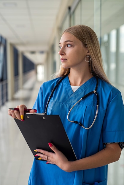 Jeune belle infirmière avec un stéthoscope autour du cou et une tablette dans les mains se tient dans le couloir de l'hôpital. Notion de médecine