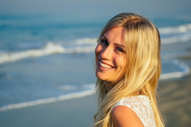 Jeune et belle mariée aux longs cheveux blonds magnifiquement souriante et marchant sur la mer dans une belle robe de mariée longue blanche. une mariée heureuse a épousé une cérémonie de mariage sur la plage au bord de la mer