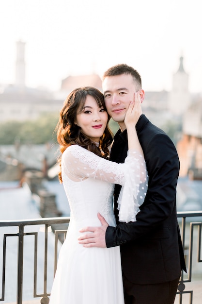 Jeune belle mariée et le marié asiatique, couple heureux au coucher du soleil dans la vieille ville européenne.