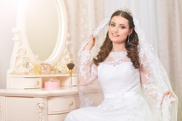 Jeune belle mariée en robe blanche posant près du miroir