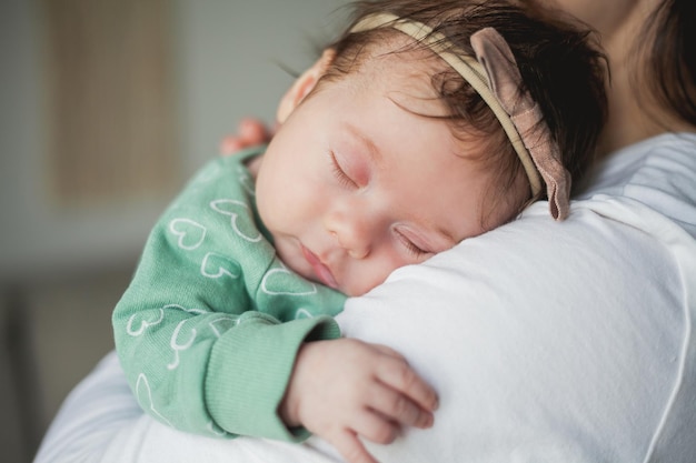 Jeune belle mère aux cheveux noirs tient sa fille nouveau-née dans ses bras dans une maison confortable Portrait de famille Maternité Jeune femme embrasse son bébé de 2 mois