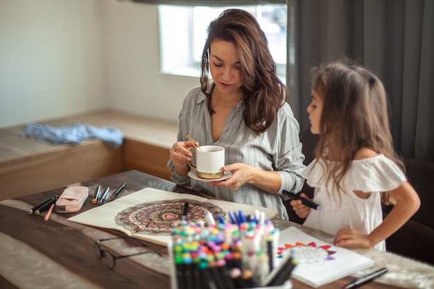 Photo la jeune belle mère et la fille mignonne dessinent un modèle de mandala ensemble des marqueurs artistiques et colore...