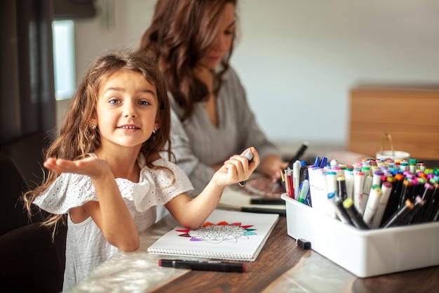 La jeune belle mère et la fille mignonne dessinent un modèle de mandala ensemble des marqueurs artistiques et colore...