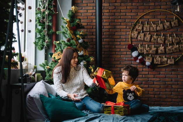 Jeune belle mère avec le fils mignon près de l'arbre de Noël avec des cadeaux. joyeux Noël