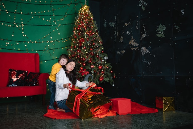 Jeune belle mère avec le fils mignon près de l'arbre de Noël avec des cadeaux. joyeux Noël