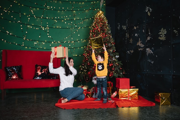 Jeune belle mère avec le fils mignon près de l'arbre de Noël avec des cadeaux. joyeux Noël