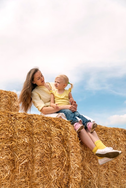 Jeune belle mère et jolie fille blonde assise dans le foin Famille heureuse sur une énorme botte de foin Récolte d'été