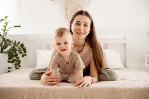 Une jeune belle mère avec un petit garçon étreignant sur le lit à la maison dans la chambre à coucher les soins et l'amour de la mère portrait d'une mère heureuse avec un enfant maternité saine