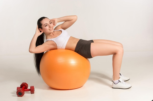 Jeune belle sportive avec des haltères s'exerçant sur le fitball