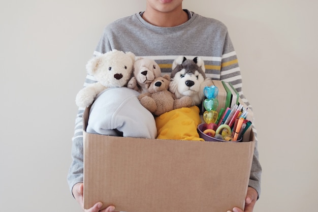 Un jeune bénévole préadolescent tenant une boîte pleine de jouets usagés.
