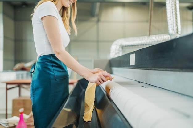 Un jeune blanchisseur tapote le linge sur la machine automatique du pressing.