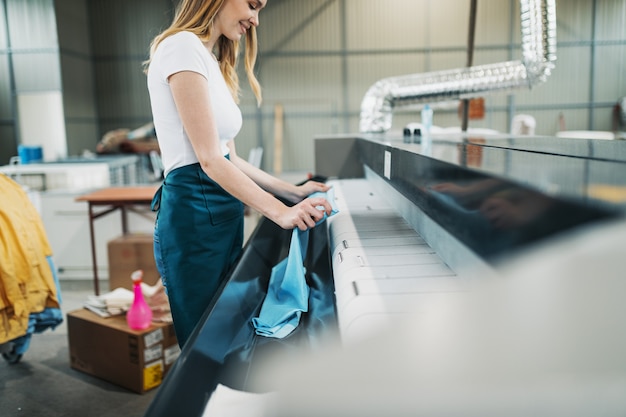 Un jeune blanchisseur tapote le linge sur la machine automatique du pressing.